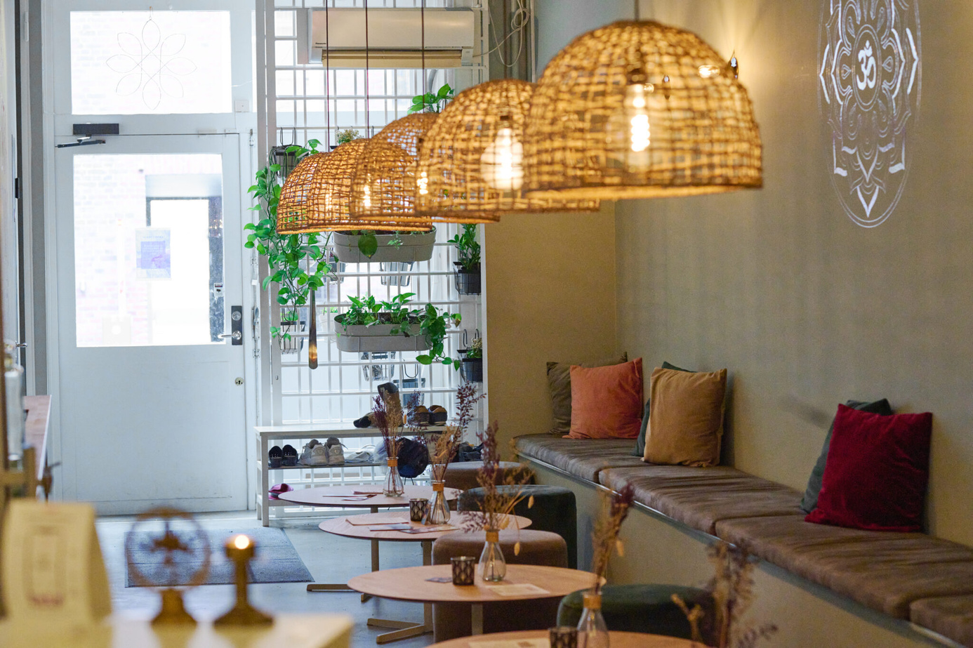 Yoga Kenda Studio Malmö seating area An indoor seating lounge with woven wicker pendant lights hanging over small round tables and benches with colorful cushions