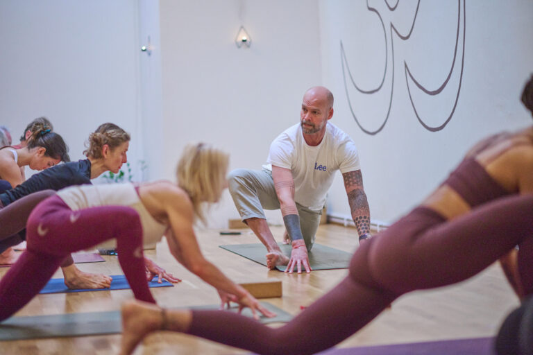 Yoga Class Kenda Malmö A yoga instructor assisting a student who is practicing a low lunge pose on a mat.